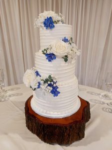 white three-tiered wedding cake with blue and white flower accents