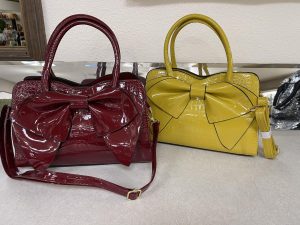 two leather purses with large bows. The one on the left is burgundy and the one on the right is yellow