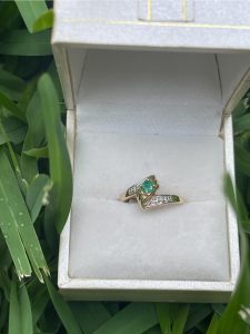 gold ring in box with green stone. The box is sitting in grass.