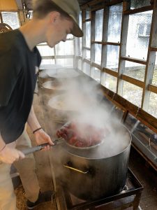 row of four pots boiling, with young man scooping crawfish through the steam