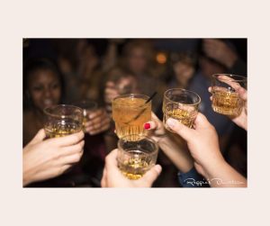 close up of five hands holding up drinks for cheers