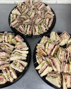 three sandwich platters with a variety of sandwiches cut into triangles