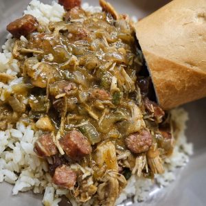 Bowl of rice with sausage and chicken gravy on top with a piece of bread on the side
