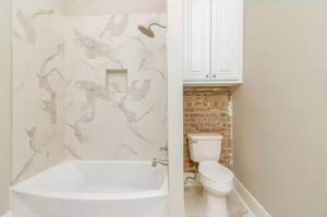 bathtub/shower combo to the left, toilet on the right with exposed brick wall