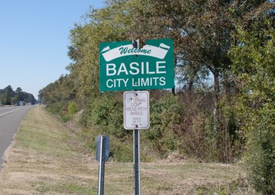 green sign on the side of the road, reads Basile City Limits