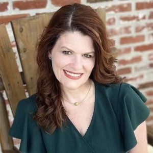 Nicole Broussard headshot with green shirt, brick wall background