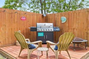 bbq and two Adirondack chairs with firepit on a small wooden deck with wooden fence in the background