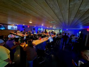 wide shot of bar scene with people leaning against the bar and standing around the room