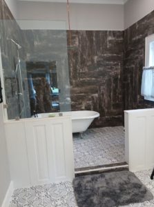 glass-surrounding tiled bathroom area with shower head and claw-foot tub