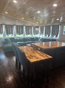 great room with island in the foreground and large couch in the background with a wall of windows