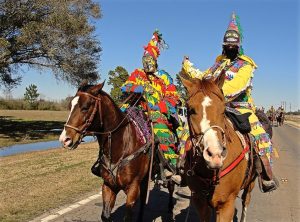 two men in traditional Mardi Gras dress riding horses on the road