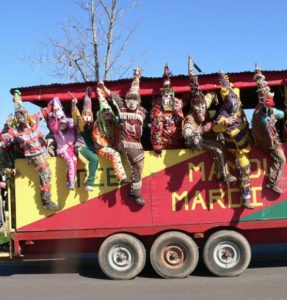 People in traditional Mardi Gras costumes hanging off parade float