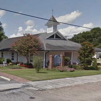 church building with crepe myrtles in front and a blue, cloudy sky