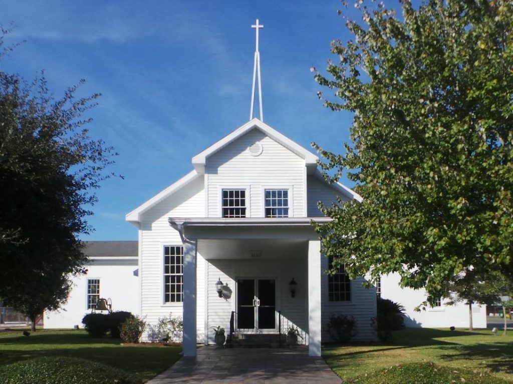 white church building with tall, thin steeple and trees out front