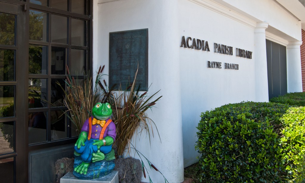 white stucco building with wood and glass front doors and a colorful frog statue