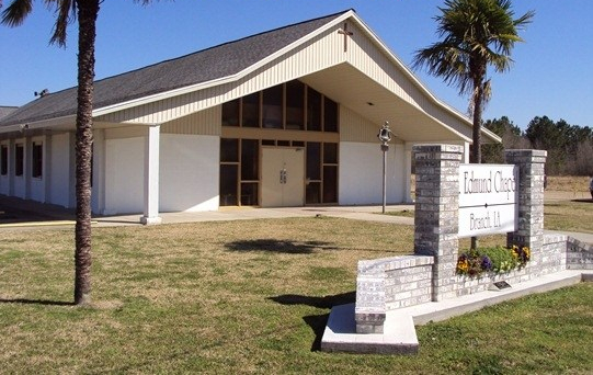 view of church with brick and stone sign out front and two palm trees