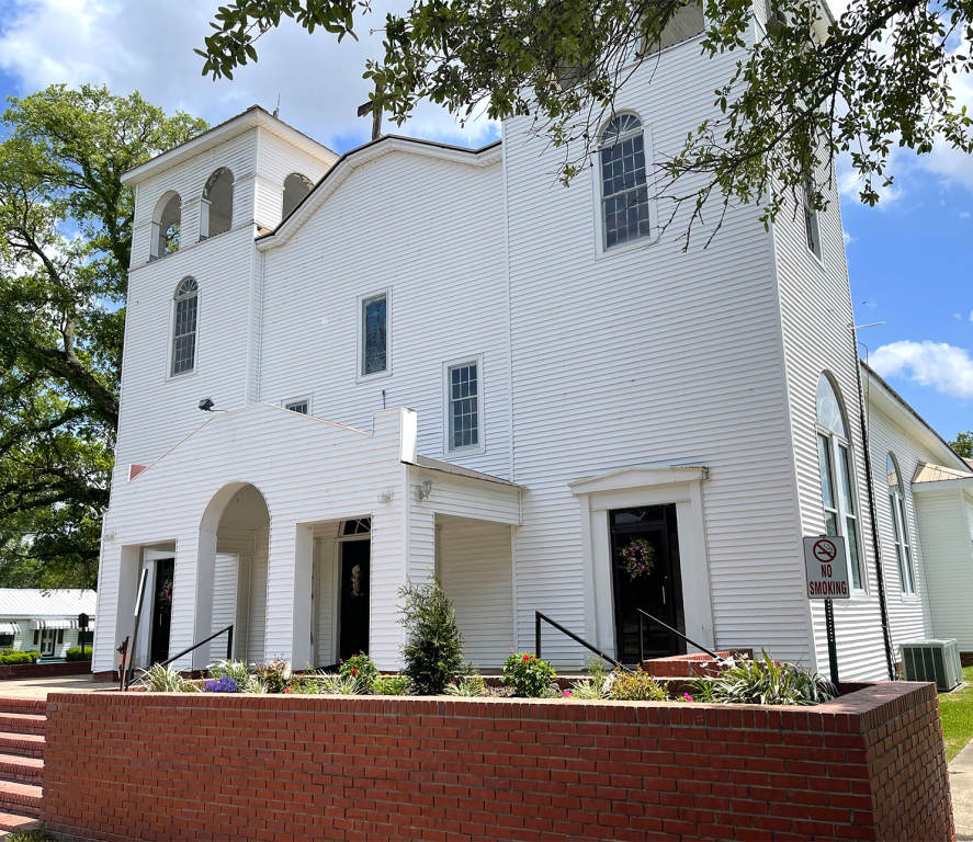 White wooden church building with brick planter out front