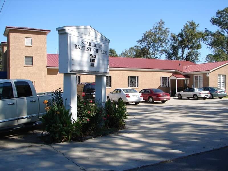 brick church building with a red roof in the background with a white church sign in the parking lot of the foreground