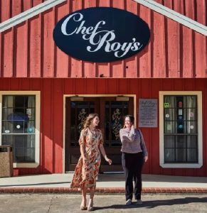 two women standing in front of a red wooden restaurant with a "Chef Roy's" sign on the front