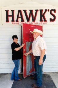 Couple opening red front door with Hawk's sign above