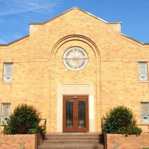 brick church building with stained glass and bushes in front