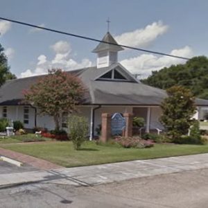 church building with crepe myrtles in front and a blue, cloudy sky