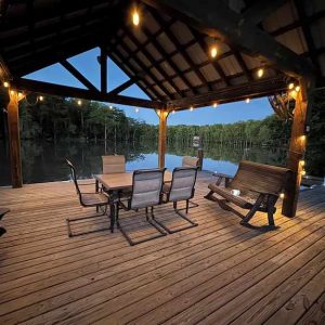 dusk photo of pavilion on the water with lights and an outdoor table and chairs