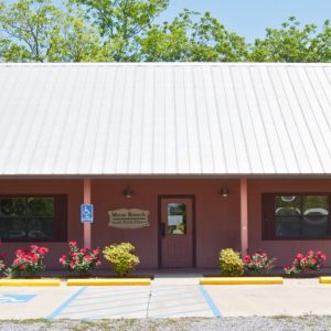 salmon-colored Acadian-style building with metal roof and flower bushes out front