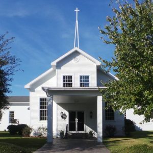 white church building with tall, thin steeple and trees out front