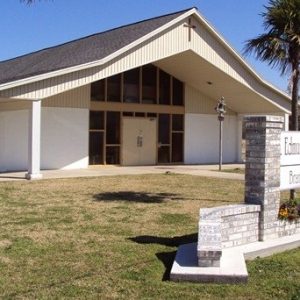 view of church with brick and stone sign out front and two palm trees